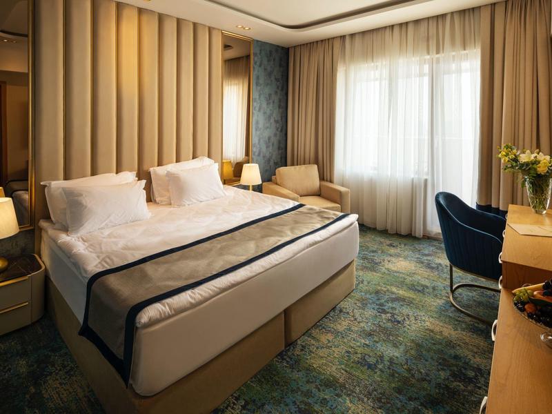 Modernes Schlafzimmer mit großem Bett, blauem Teppich, Vorhängen und Schreibtisch am Fenster.