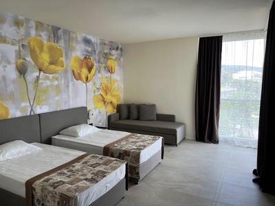 Hotelzimmer mit zwei Einzelbetten, grauem Sofa und großer Fensterfront mit Blick nach draußen.