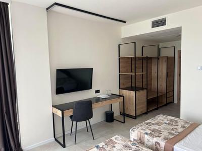 Modernes Hotelzimmer mit Schreibtisch, Stuhl, Fernseher und offenem Kleiderschrank in neutralen Farben.