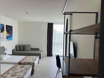 Modernes Hotelzimmer mit zwei Betten, Sofa, Schreibtisch und Fenster mit Vorhang.