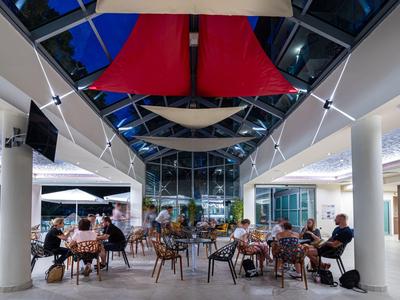 Modernes Hotelrestaurant mit geöffnetem Dach, roten Segeln und Gästen an Tischen