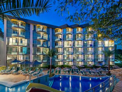 Modernes Hotel mit Pool und Balkonen, umgeben von Palmen bei Abenddämmerung.