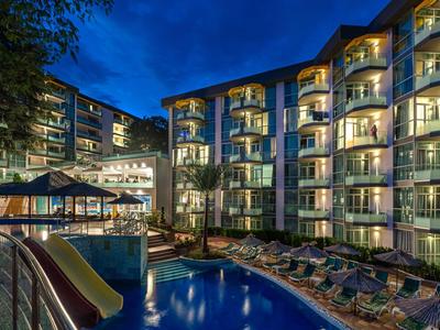 Beleuchtetes Hotel mit Pool und Liegestühlen bei Nacht.