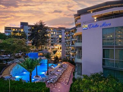 Hotelanlage mit beleuchtetem Pool bei Sonnenuntergang und angrenzenden Gebäuden.