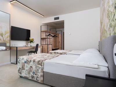 Modernes Hotelzimmer mit zwei Einzelbetten, Fernseher, Schreibtisch und offener Kleiderablage.