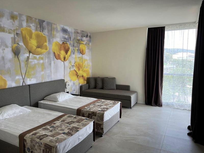 Hotelzimmer mit zwei Einzelbetten, grauem Sofa und großer Fensterfront mit Blick nach draußen.