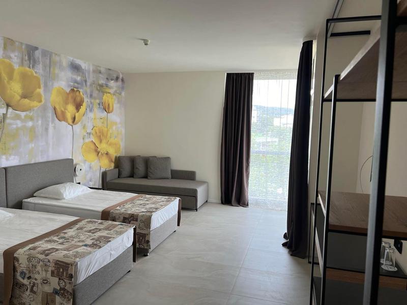 Modernes Doppelzimmer mit zwei Einzelbetten, Sofa und großem Fenster mit Vorhängen.