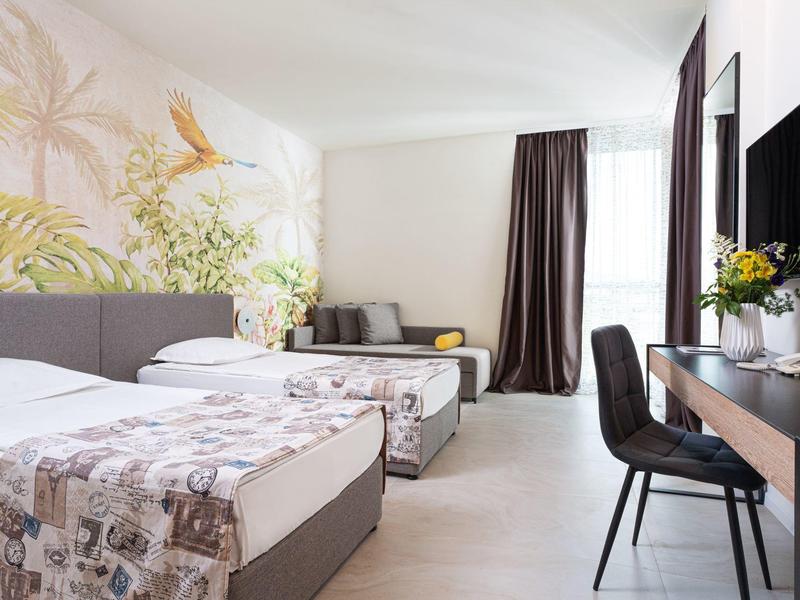 Hell eingerichtetes Hotelzimmer mit zwei Einzelbetten, Sitzbereich und Schreibtisch.