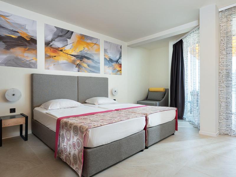 Modern eingerichtetes Hotelzimmer mit zwei Einzelbetten, Nachttischen und Balkon mit Blick nach draußen.