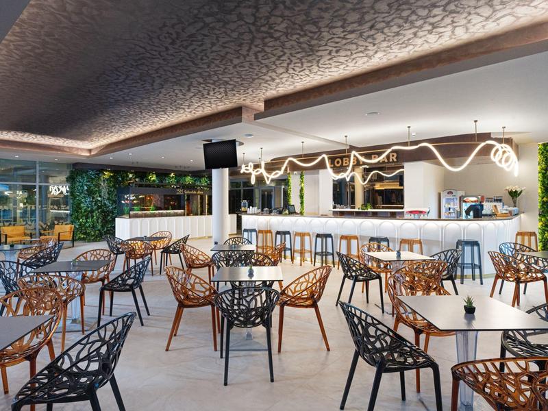 Moderner Außenbereich einer Bar mit eleganten Tischen und Stühlen, inklusive Barbereich und Grünpflanzen.