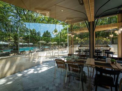 Ein heller Hotelterrassenbereich mit Stühlen und Tischen, umgeben von Glaswänden und Bäumen im Hintergrund.