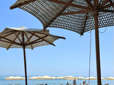 Sonnenschirme und Stühle in einem Außenbereich mit Blick auf einen Strand und das Meer.