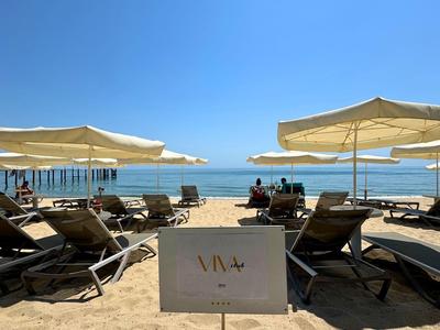 Sonnenschirme und Liegestühle am Sandstrand mit Blick auf das Meer bei klarem Himmel.
