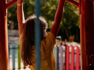 Kind klimt aan een rode klimstang op een zonnige dag op een speeltuin