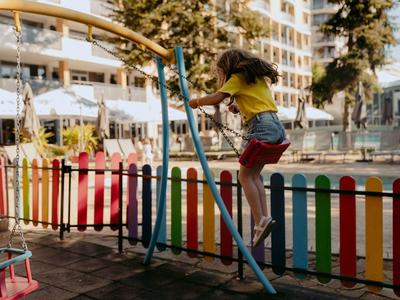 Kind schommelt op een kleurrijke speeltuin naast een hotelgebouw.