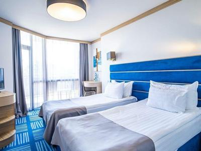 Hotelkamer met twee eenpersoonsbedden, blauw hoofdeinde en aan de muur gemonteerde tv.