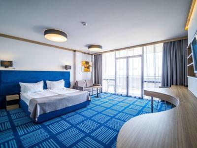 Modern ingerichte hotelkamer met groot bed, blauw tapijt en panoramische ramen.