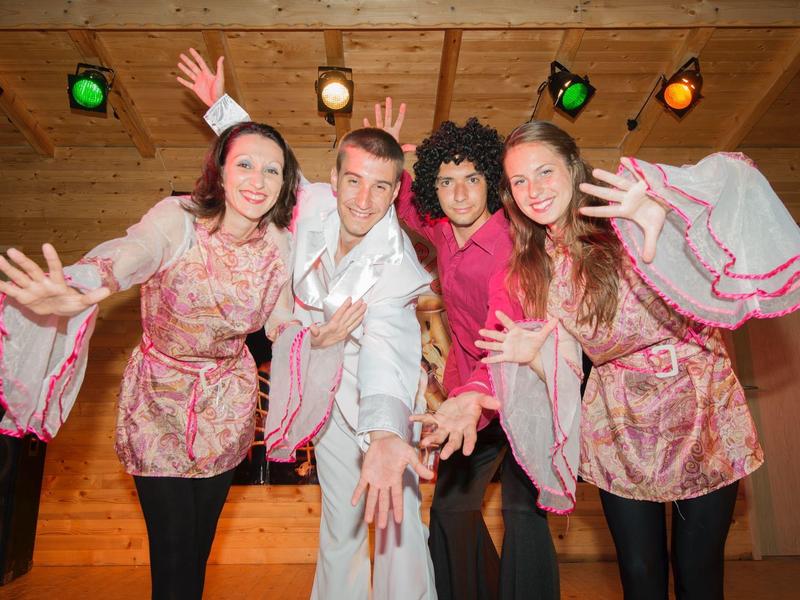 Vier personen in kleurrijke kleding poseren vrolijk binnen een ruimte met houten wanden.