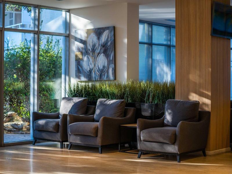 Gezellige zithoek met banken en stoelen naast grote ramen in een lichte hotelruimte.