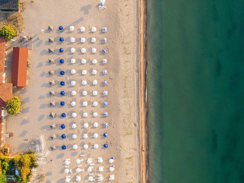 Luchtfoto van een strandhotel met parasols, zandstrand en helder zee.