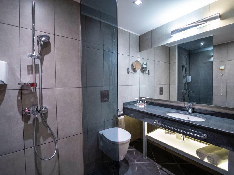 Moderne badkamer met douche, toilet, grote spiegel en wastafel op een zwart aanrecht.