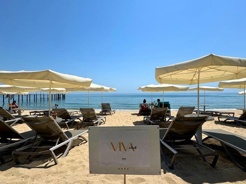 Zandstrand met ligstoelen en parasols onder een blauwe lucht bij de zee