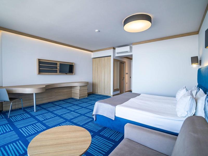 Modern hotelkamer met twee bedden, bureau en blauw tapijt.