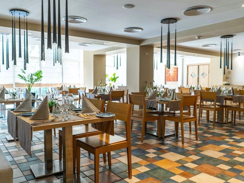 Licht restaurant met houten tafels, kleurrijk betegelde vloer en moderne hanglampen.