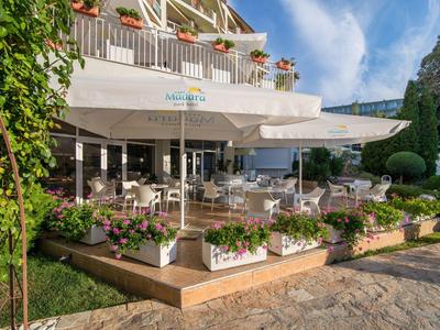 Terrassenrestaurant mit weißen Tischen, bunten Blumen und großen Sonnenschirmen bei blauem Himmel.