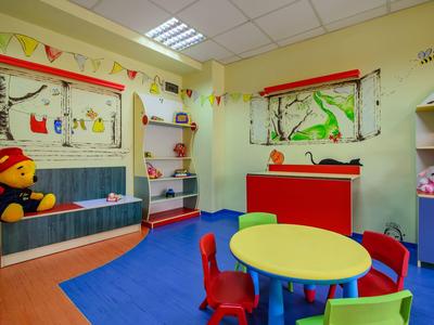 Sala de juegos infantil colorida con mesas redondas, sillas pequeñas y decoración de paredes en un hotel.