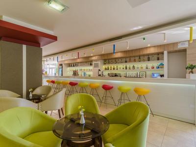 Moderne Hotelbar mit farbigen Barhockern und gemütlichen Sitzbereichen in grün und beige.