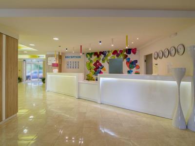 Recepción moderna de hotel con mostrador blanco, mural colorido y suelo de mármol claro.