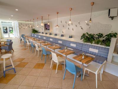 Helles, modernes Restaurant mit langen Sitzreihen und blauen sowie weißen Stühlen