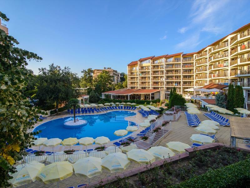 Gran piscina de hotel con muchas sombrillas y tumbonas bajo un cielo azul.