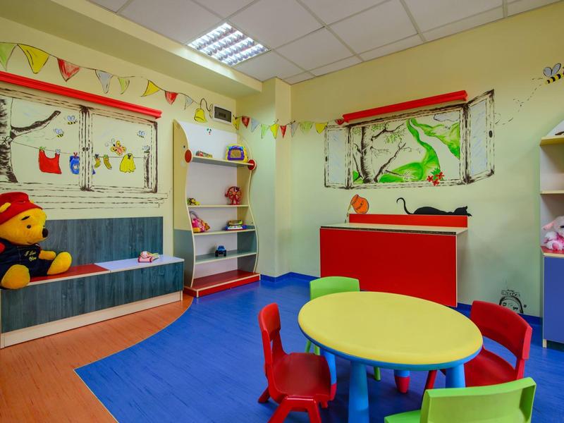 Sala de juegos infantil colorida con mesas redondas, sillas pequeñas y decoración de paredes en un hotel.