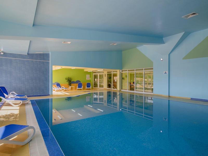 Piscina interior bien iluminada con sillas azules y paredes verdes.