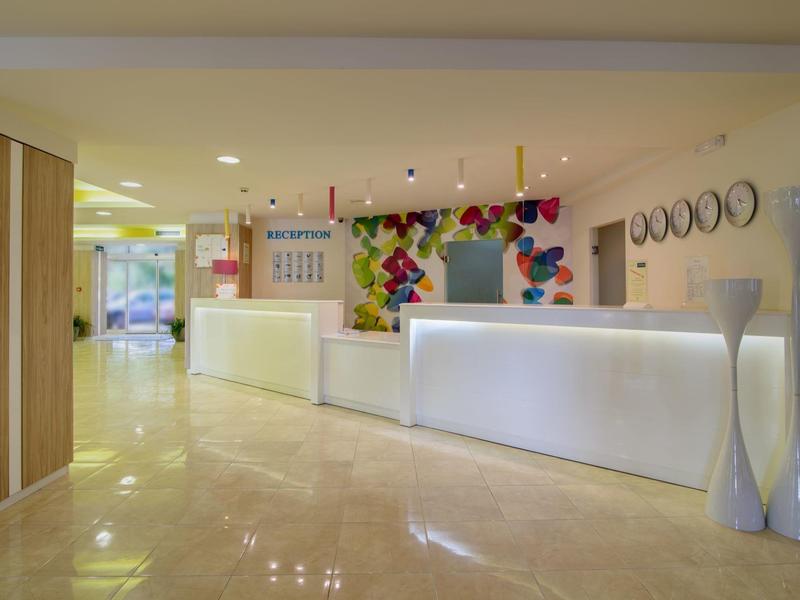 Recepción moderna de hotel con mostrador blanco, mural colorido y suelo de mármol claro.