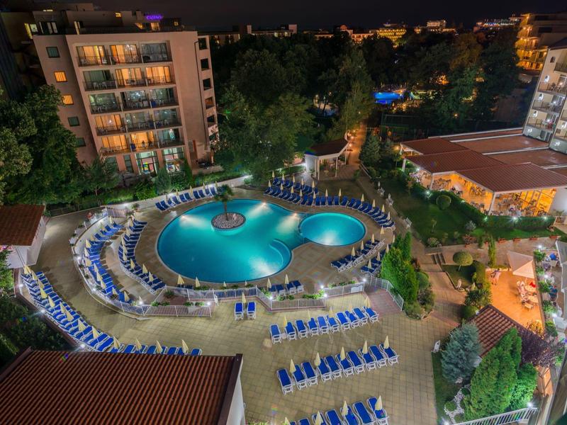 Piscina iluminada del hotel con tumbonas y rodeada de edificios en una foto nocturna.