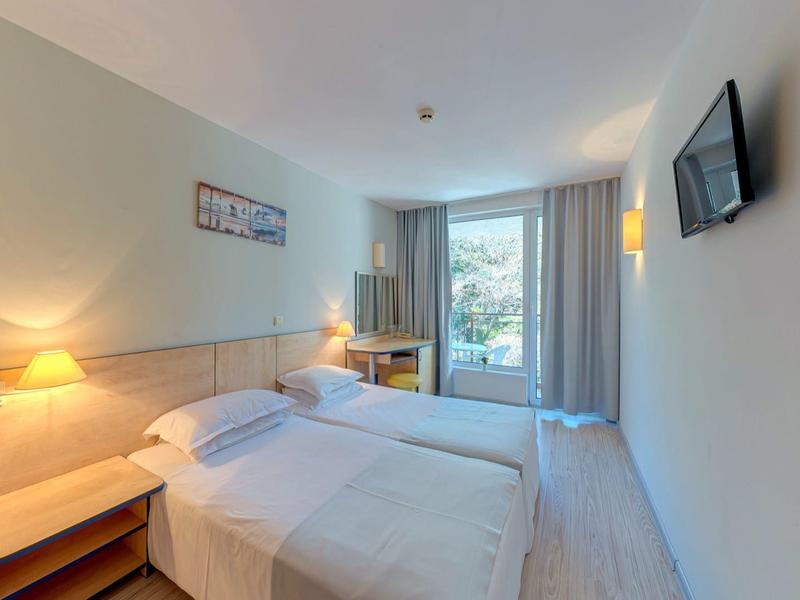 Habitación de hotel luminosa con cama doble, mesitas de noche y televisor en la pared.