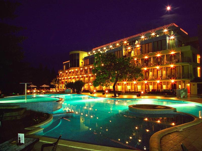 Osvětlená hotelová budova s bazénem v noci, obklopená stromy.