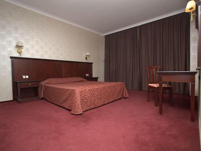 Einfaches Hotelzimmer mit Doppelbett, braunem Teppich und Vorhängen sowie einem kleinen Schreibtisch.