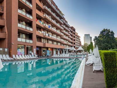 Großer Außenpool neben einem mehrstöckigen Hotelgebäude mit Sonnenliegen und Schirmen im Freien.
