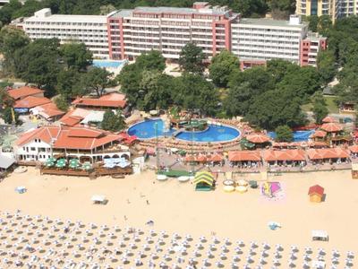 Großer Sandstrand mit vielen Liegestühlen und Hotels im Hintergrund, umgeben von grünen Hügeln.