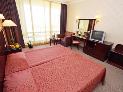 Hell eingerichtetes Hotelzimmer mit zwei Betten, Fernseher, Fensterfront und gemütlichem Sitzbereich.