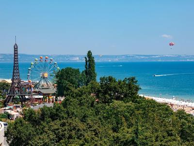Küstenstadt mit Strand, grün bewachsenen Hügeln, kleiner Eiffelturm-Nachbildung und einem Riesenrad.