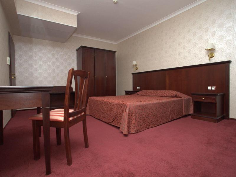 Einfaches Hotelzimmer mit Doppelbett, rotem Teppich, Holzmöbeln und gemusterten Tapeten.