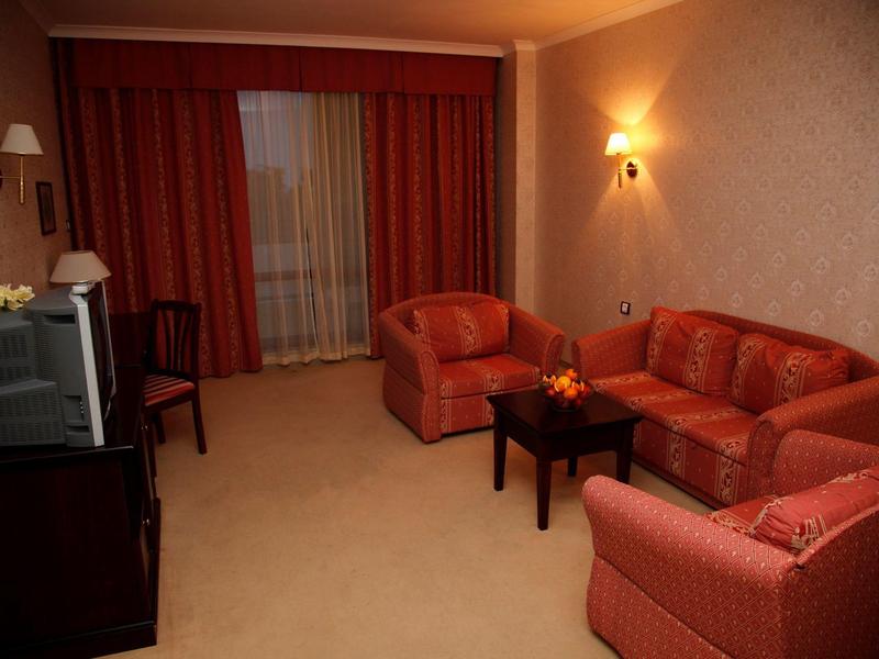 Gemütliches Wohnzimmer mit rotem Sofa, Sesseln, kleinem Holztisch und TV auf dunklem Schrank.