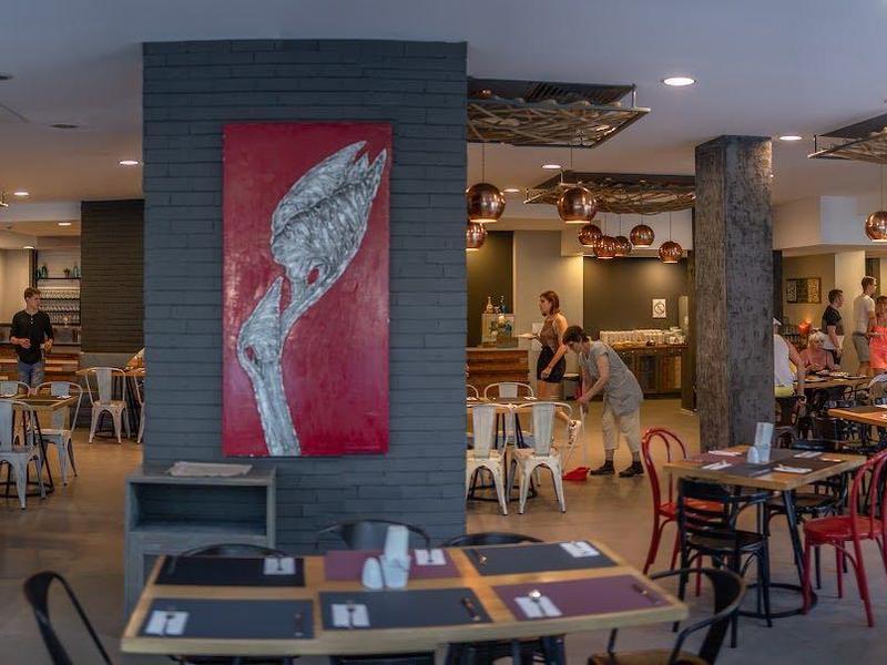 Modernes Restaurant mit Holz- und Metallstühlen, Tischen, grauem Boden und roter Wanddekoration.