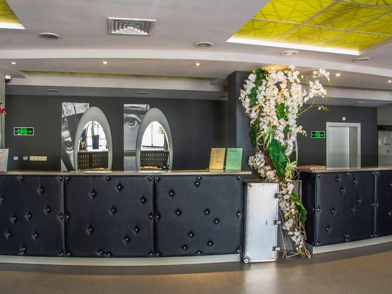 Moderner Empfangstresen mit schwarzen Polstern, Blumenarrangement und gelbem Deckendesign.