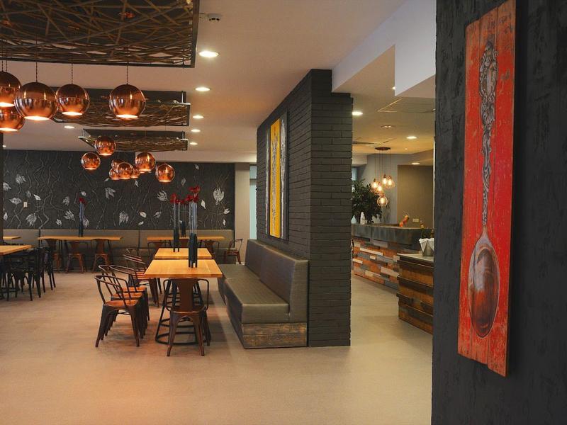 Moderner Gastraum mit Holztischen, Kupferlampen und gedeckten Farben, Betonboden, rote Kunst an Wand.